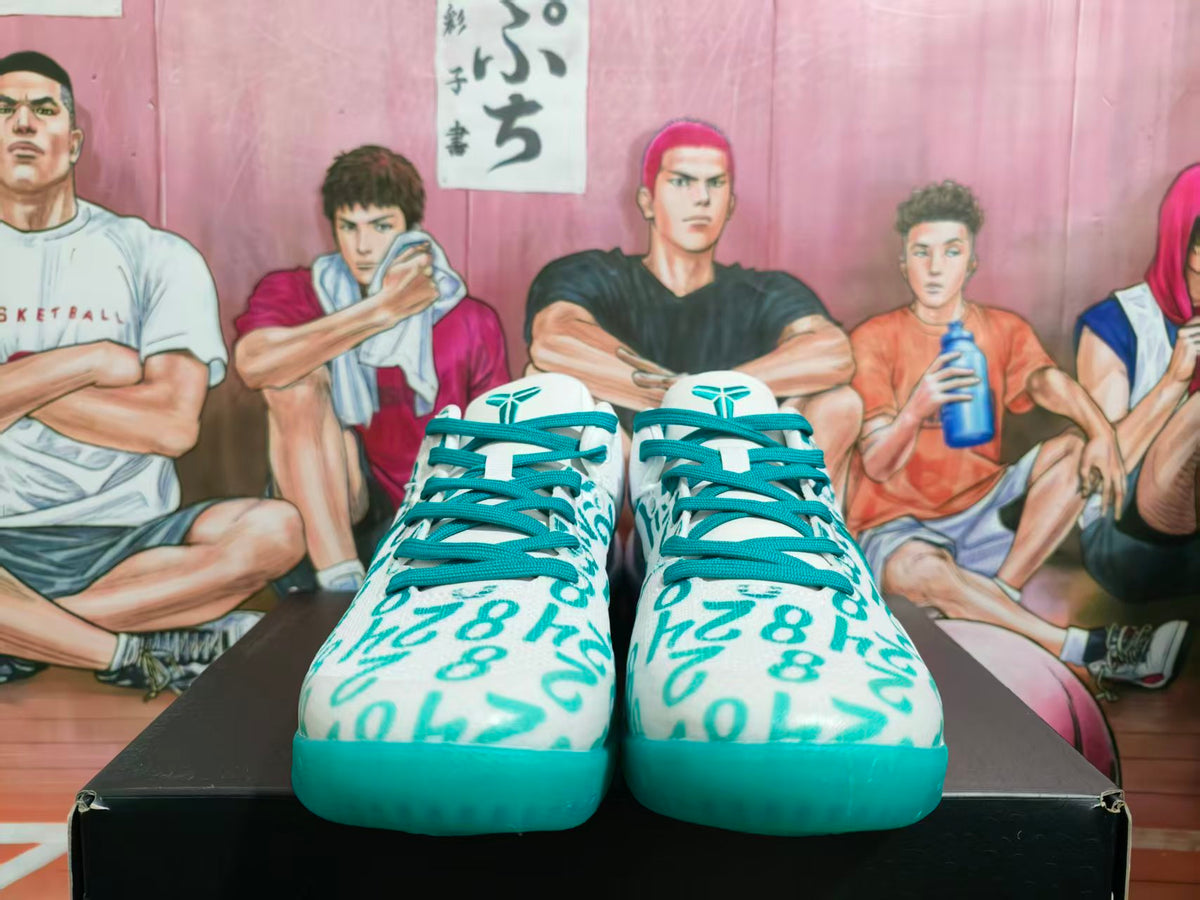 Front view of white and lake-green Nike basketball sneakers with teal laces and patterned uppers on a black shoebox.