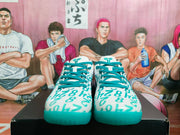 Front view of white and lake-green Nike basketball sneakers with teal laces and patterned uppers on a black shoebox.
