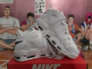 Angled view of the paired white Nike sneakers highlighting the layered side construction, AIR lettering and dark cushioning windows.