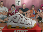 Side view of a white Nike basketball sneaker with burgundy-outlined AIR lettering and a segmented gum-colored sole.