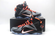 Pair of black, grey and orange high-top basketball sneakers displayed on and in front of a black shoe box.