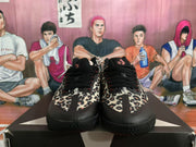 Front view of black sneakers with leopard-print uppers, black laces, and textured outsoles.