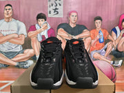 Front view of black Nike sneakers showing the lace-up design, textured uppers, padded collars, and orange tongue details.