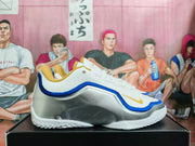 Side view showing a white Nike shoe with a blue accent line, metallic silver heel panel, and gold logo.