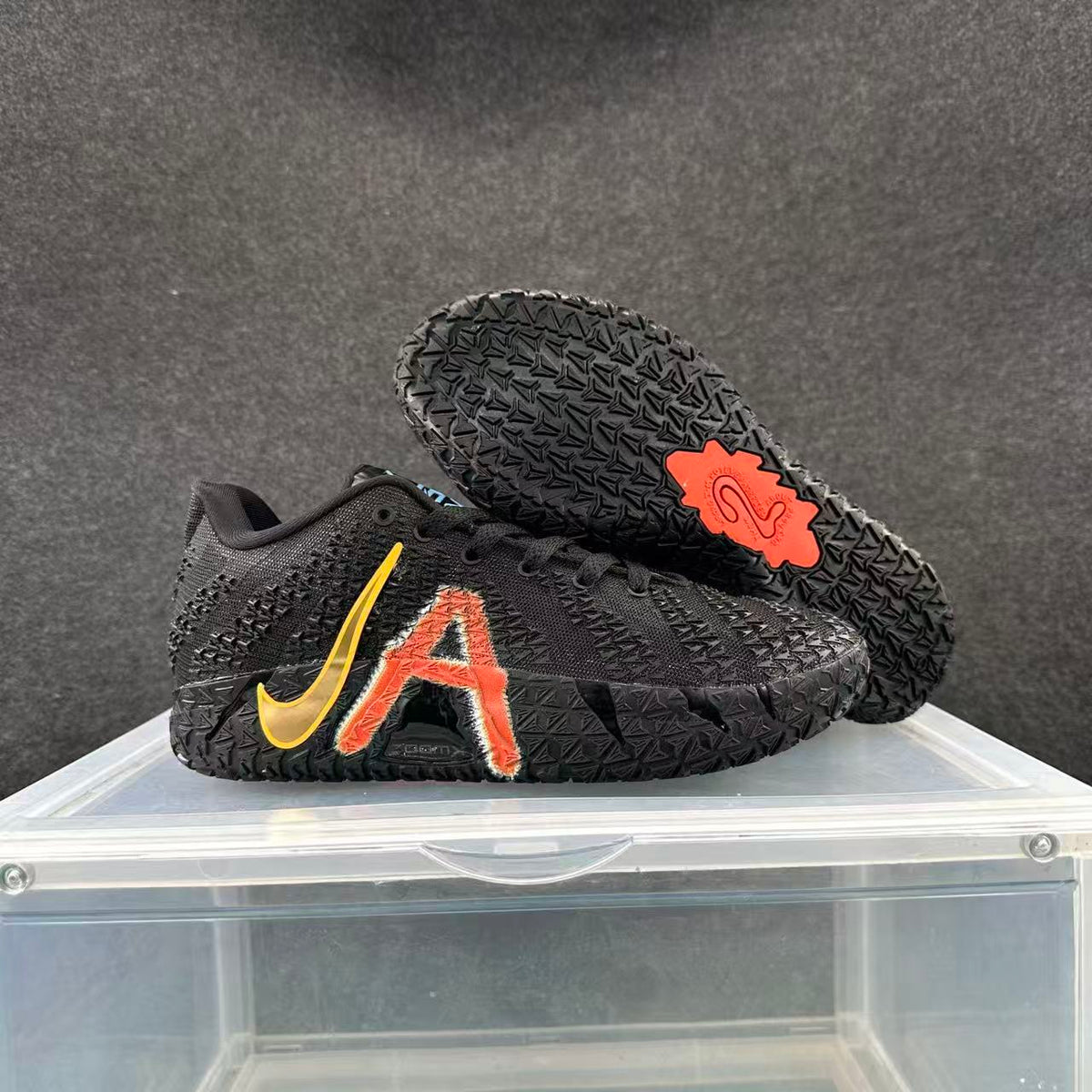 Black Nike basketball shoe with red-orange side graphic and gold-colored Swoosh, shown beside its patterned outsole