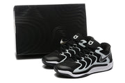 Paired sneakers displayed beside a black box, showing the black and white color scheme and patterned outsole.