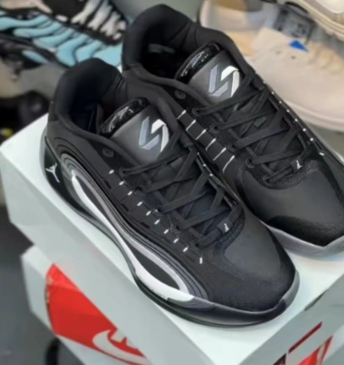 Pair of black and white low-top sneakers with layered side panels, padded collars, and contrasting outsole details, shown on a shoebox.