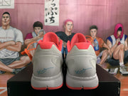 Rear view of blue-grey Nike basketball sneakers with orange-red collars and heel details, displayed on a black shoebox.