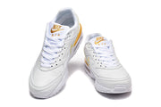 Front view of white Nike Air Max sneakers with gold tongue details.
