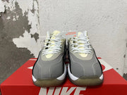 Front view of grey Nike sneakers with white laces and pale yellow accents