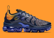 Side profile showing the gray-purple upper, navy wavy overlays, orange heel panel, and segmented blue sole.