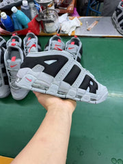 Gray and black Nike sneaker held above a worktable, with matching sneakers visible in the background.