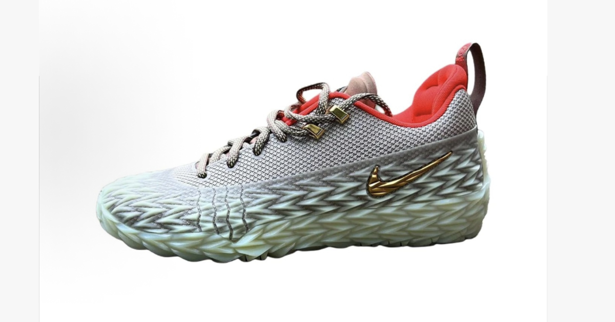 Gray low-top Nike basketball shoe with a patterned sole, red lining, and gold-tone Swoosh