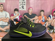 Side view of a black basketball sneaker showing the textured upper, bright yellow-green swoosh, purple outsole, and matching laces.