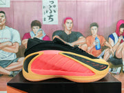 Side profile of a black Adidas basketball shoe with coral-pink panels and gold-toned trim.