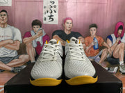 Front view of the pair showing white textured uppers, white laces, black tongue logos, and yellow outsoles.