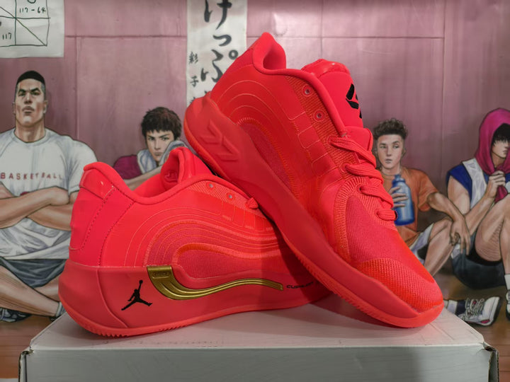 Pair of red Jordan basketball sneakers with gold-tone side detailing shown on a shoebox.