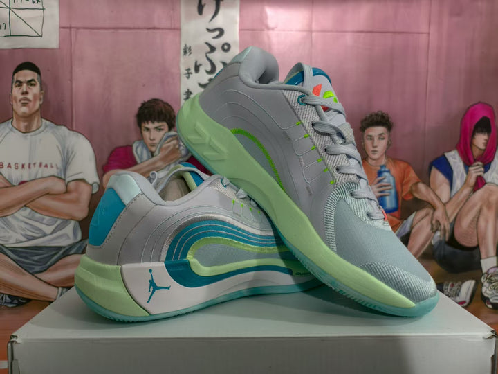 Pair of light gray Jordan basketball sneakers with blue and green accents displayed on a box.