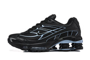 Side view of a black Nike Shox R4 sneaker with light blue accents and circular heel columns.
