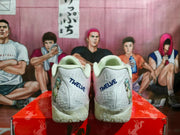 Rear view of the sneakers showing white heels with blue “TWELVE” lettering, illustrated side panels and textured outsole details.