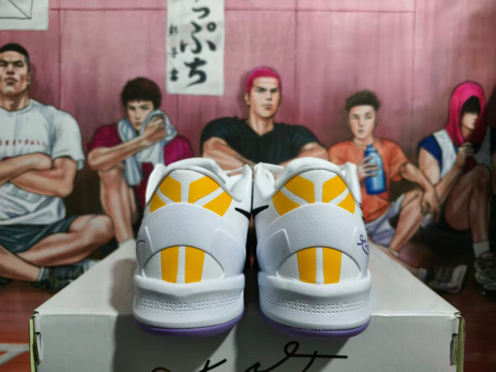 Rear view of white sneakers with yellow heel accents, purple outsoles, and black-and-purple detailing.