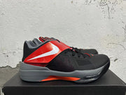 Side view of black and red basketball shoes with a gray midsole and prominent strap