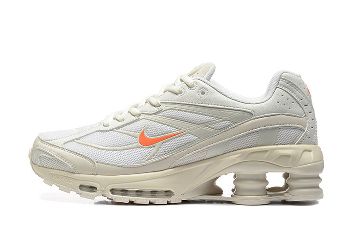 Side view of light-colored Nike Shox Ride 2 sneakers with orange accents and column-shaped heel cushioning.