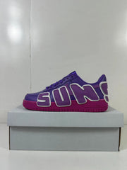 Side view of purple low-top sneakers with oversized AIR lettering and a magenta outsole on a box.
