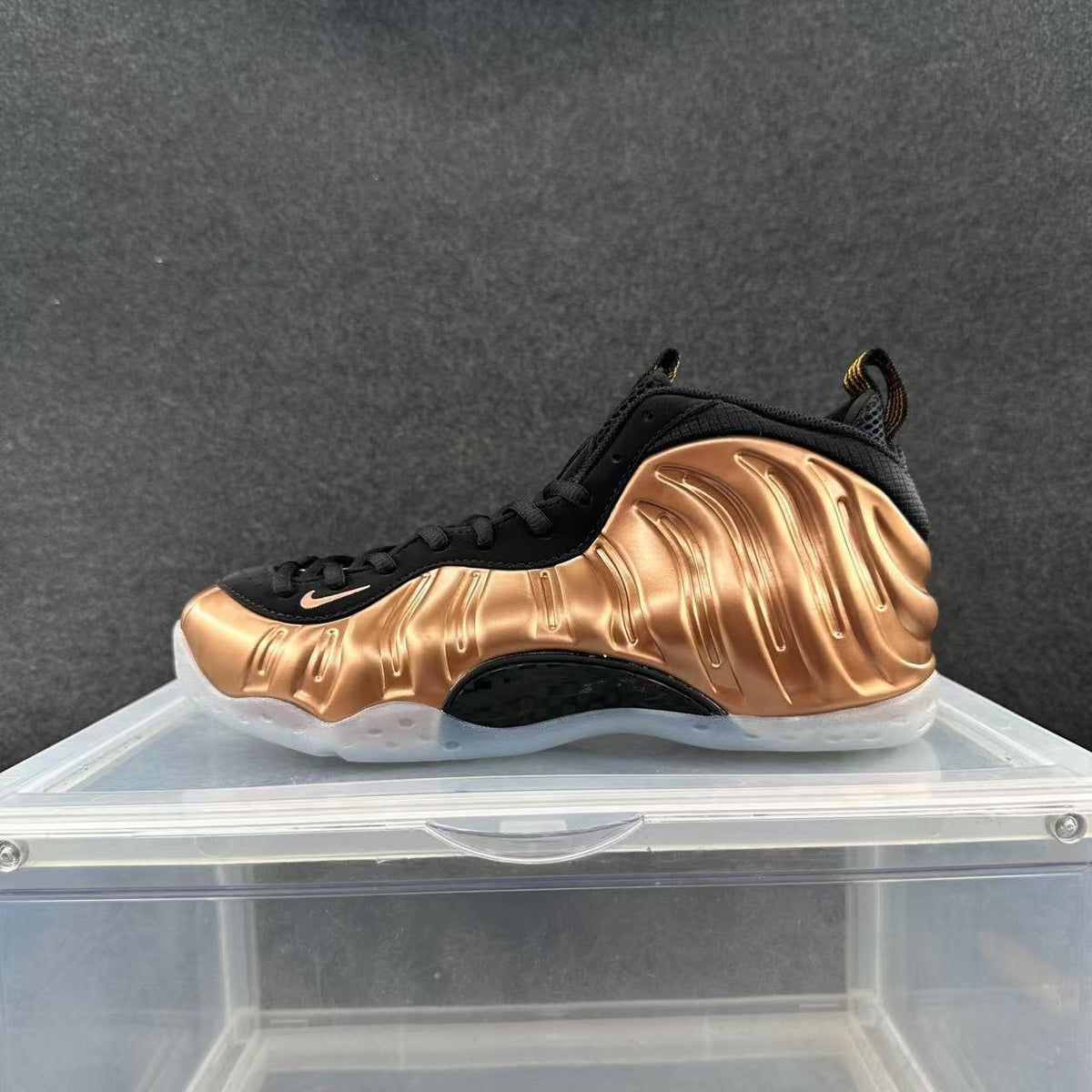 Side view of a black and metallic copper Nike Foamposite-style high-top sneaker with a translucent-looking outsole.