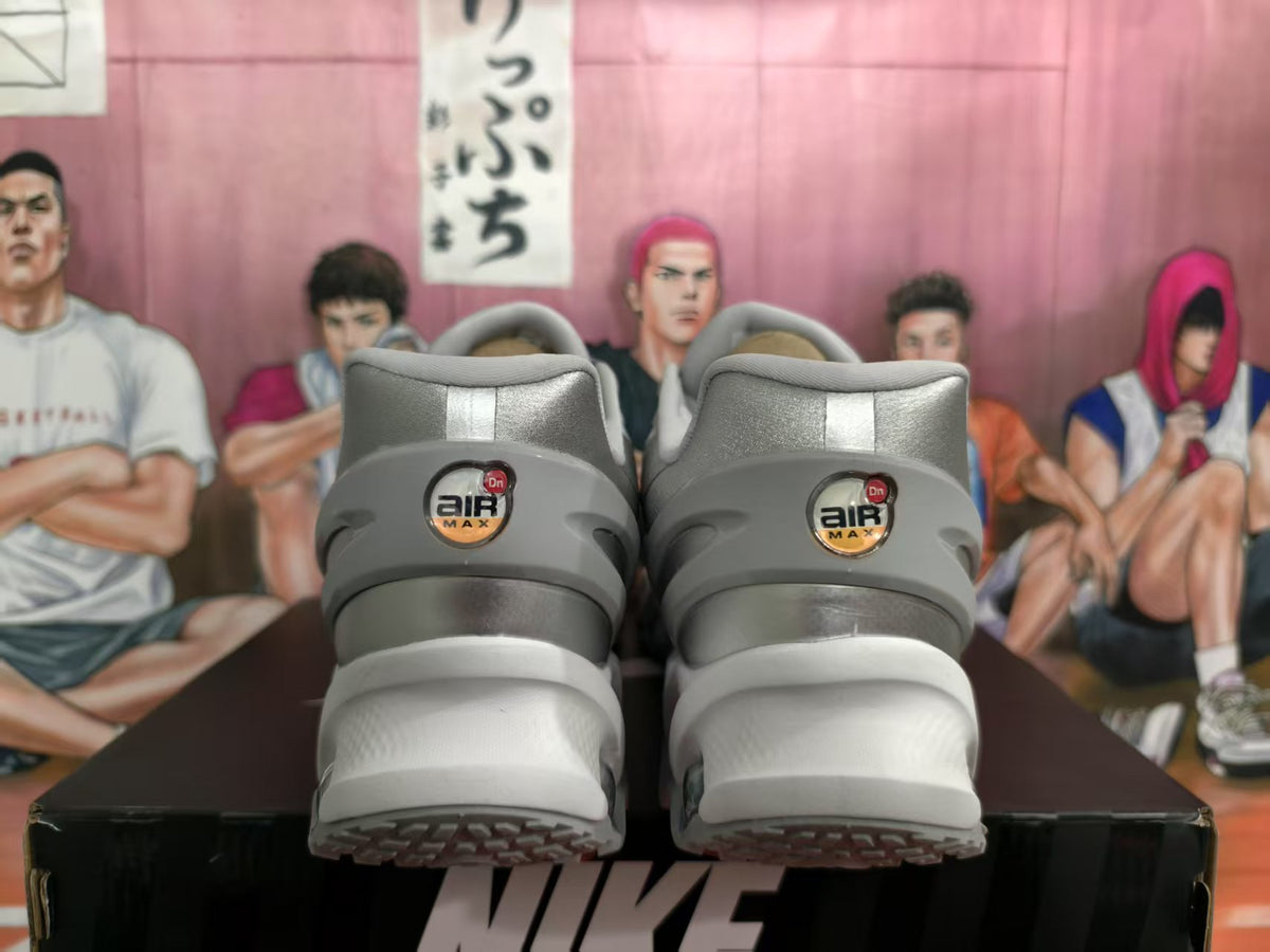 Rear view of silver Nike sneakers showing Air Max Dn heel branding and layered white-gray soles.