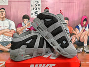 Angled view of the gray and black Nike sneaker pair highlighting the layered side panels, red pull tabs, and transparent midsole cushioning.