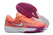 Two coral sneakers shown from the side and outsole, highlighting the purple patterned tread and white midsole.