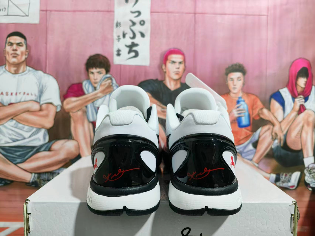 Rear view of white Nike basketball sneakers with glossy black heel panels, red script details, and black-and-white soles on a shoebox.