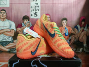 Angled view of the orange-red Nike sneakers showing both shoes, the textured side panels, green laces, and translucent soles.