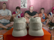 Rear view of white Nike sneakers with embossed heel branding and red outsoles on an orange box.