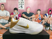Side view of a white Nike Kobe basketball shoe with a gold swoosh and gold heel panel