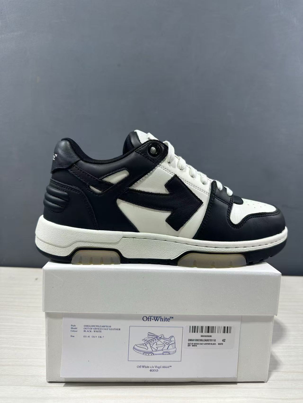 Side view of black-and-white Off-White Out Of Office sneakers displayed on a shoebox; the box label shows sample size EU 42 and style code OMAI89C99LEA0070110.