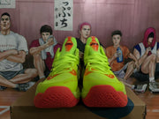 Front and outsole view of lemon-yellow ASICS basketball shoes showing orange-red toe sections and textured soles.
