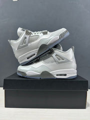 Pair of grey Jordan Air Jordan 4 sneakers arranged on a black shoebox, showing both lateral sides and the outsole edge.