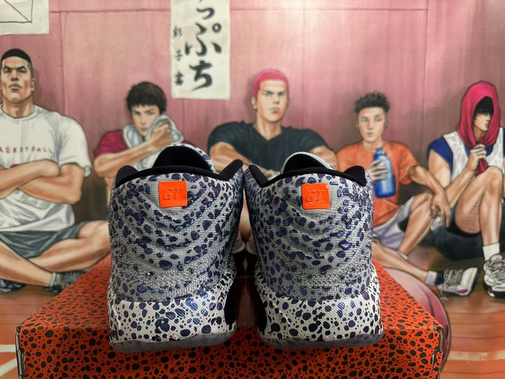 Rear view of gray Nike basketball shoes with blue and black speckling and orange heel tabs.