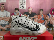 Side view of a white Nike Air More Uptempo sneaker with black accents and prominent side lettering.
