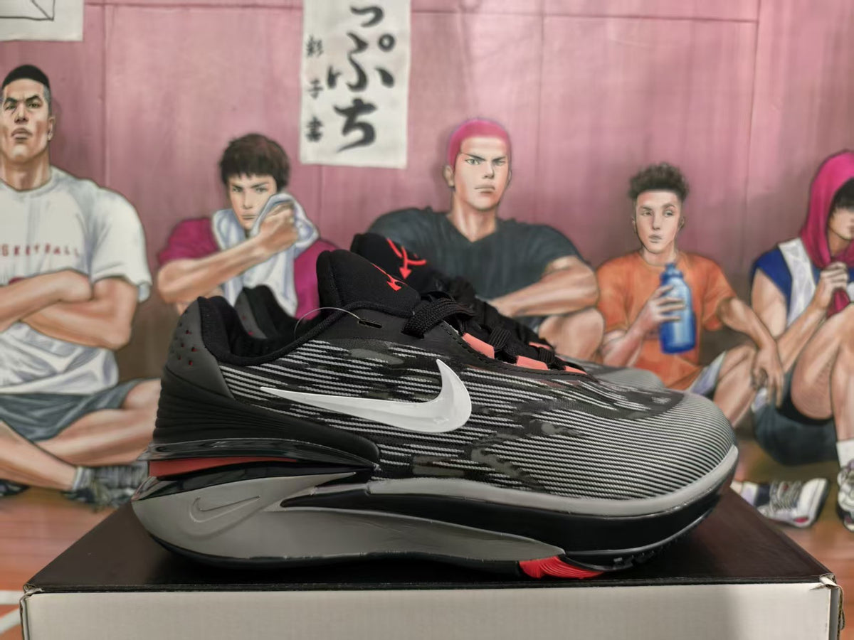 Side view of black and gray Nike sneakers with a white side swoosh and red sole accents on a box.