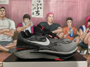 Side view of black and gray Nike sneakers with a white side swoosh and red sole accents on a box.