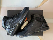 Pair of black high-top basketball shoes displayed at an angle with a box and spare laces.
