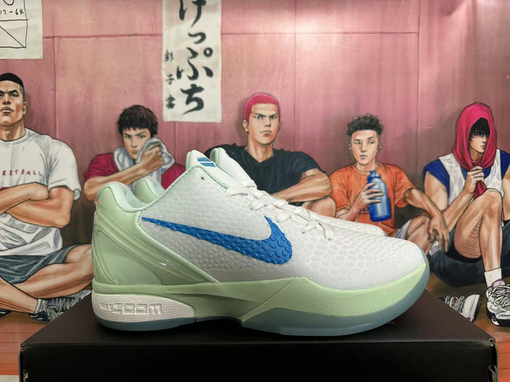 Side view of a white low-top Nike basketball shoe with a blue side logo and pale sage-green heel and sole accents.