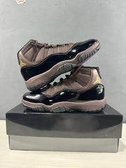 Two black and bronze Air Jordan 11 Retro sneakers arranged on a shoebox.