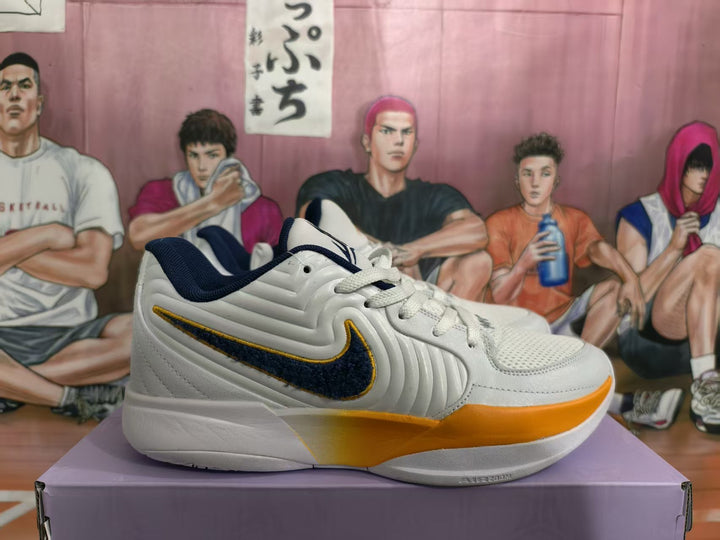Side view of white Nike basketball sneakers with navy side detailing and orange sole accents on a shoebox.