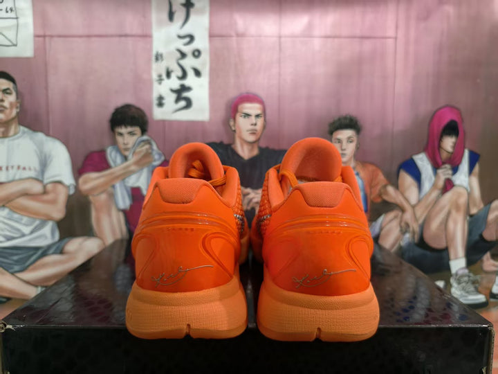 Rear view of a pair of bright orange Nike basketball sneakers showing padded collars, orange midsoles, and signature-style heel graphics.