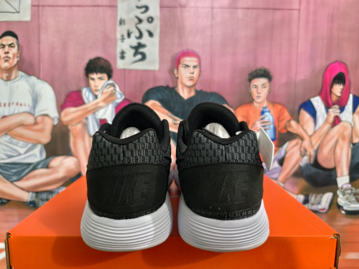 Rear view of a pair of black Nike sneakers showing textured heel panels and white ridged soles on an orange box.