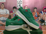 Angled view of two green Jordan sneakers displaying the low-top shape, tonal upper, white midsoles, and light gum-colored outsoles.